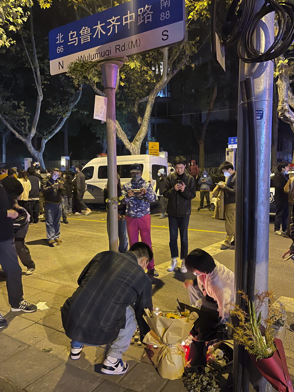 FILE - People mourn for the victims of a recent deadly fire at a residential building in Urumqi city at a road sign of the Middle Wulumuqi Road or Middle Urumqi Rd in Shanghai, China on Nov. 26, 2022. What started as an unplanned vigil last weekend in Shanghai by fewer than a dozen people grew hours later into a rowdy crowd of hundreds. The protesters expressed anger over China's harsh COVID-19 policies that they believed played a role in a deadly fire on Nov. 24 in a city in the far west. (AP Photo, File)