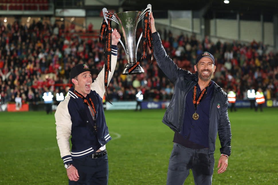 Wrexham owners Rob McElhenney and Ryan Reynolds hold the Vanarama National League Trophy as Wrexham celebrate promotion back to the English Football League during the Vanarama National League match between Wrexham and Boreham Wood at Racecourse Ground on April 22, 2023 in Wrexham, Wales.