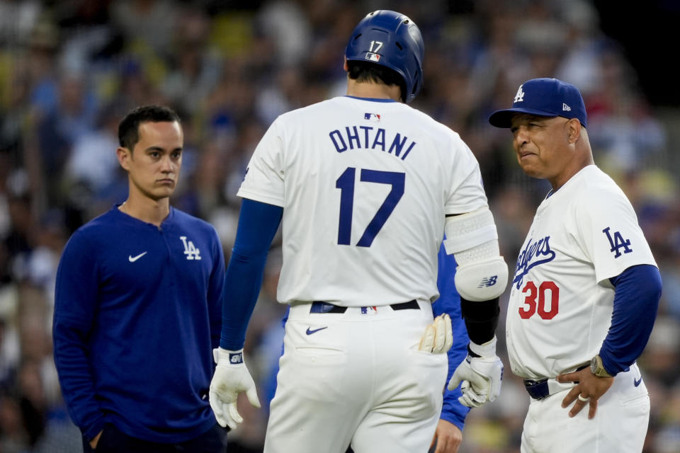 Los Angeles Dodgers designated hitter Shohei Ohtani, front center, speaks with interpreter Will Ireton, head athletic trainer Thomas Albert, and manager Dave Roberts, from left, after being hit by a foul tip during the third inning of a baseball game against the Arizona Diamondbacks, Tuesday, July 2, 2024, in Los Angeles. (AP Photo/Ryan Sun)