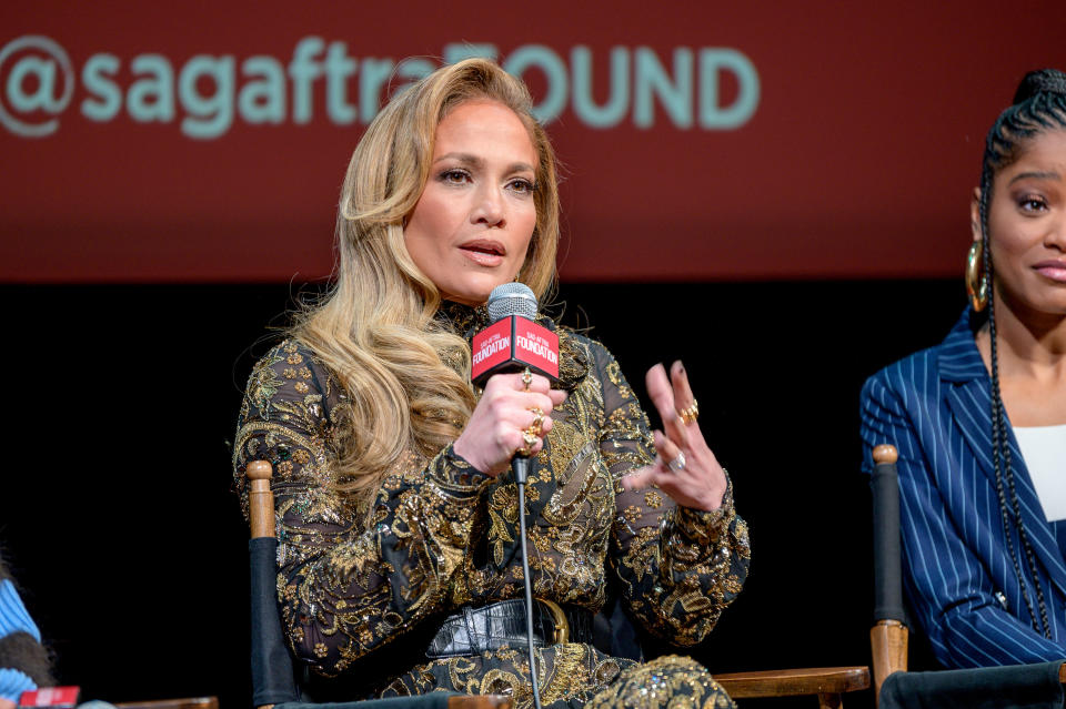 JLo sitting and holding a microphone