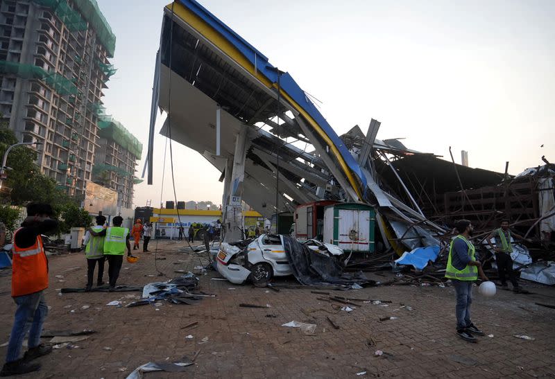 Members of rescue teams stand at a damaged fuel station after a massive billboard fell during a rainstorm in Mumbai