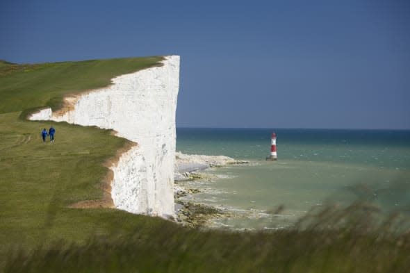 A couple walking along the clifftop of the dramatic coastline at Beachy Head., Beachy Head, East Sussex, England. Additional Cre