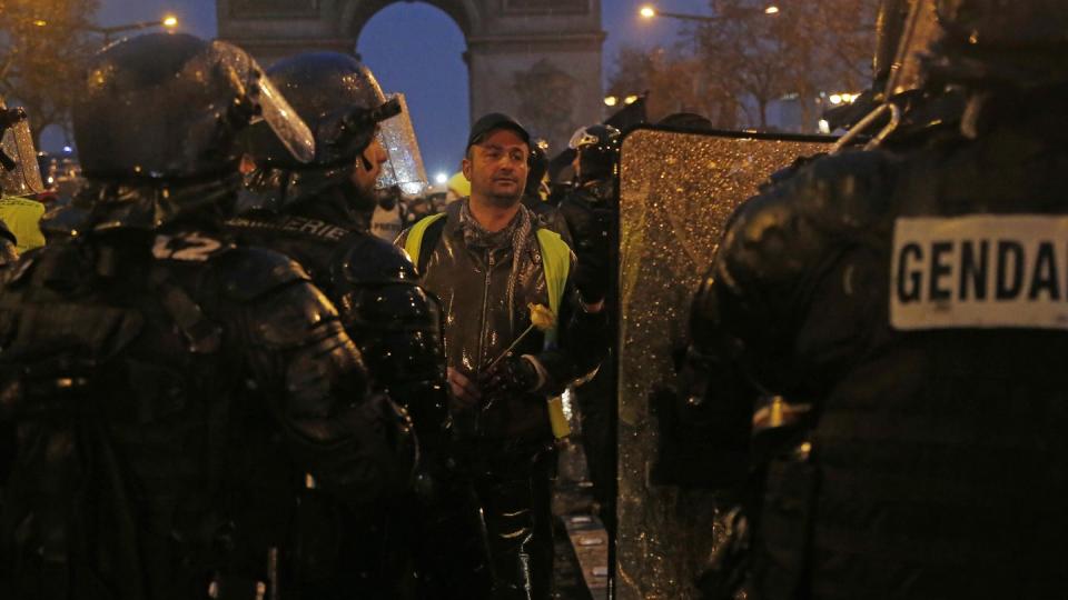 Ein «Geldwesten»-Demonstrant mit einer Blume in der Hand vor Bereitschaftspolizisten. Um den Konflikt mit den «Gelbwesten» zu entschärfen, versprach Macron zu Wochenbeginn ein Paket mit Sofortmaßnahmen im Sozialbereich, darunter eine Erhöhung des Mindestlohns um monatlich 100 Euro. Foto: Michel Euler