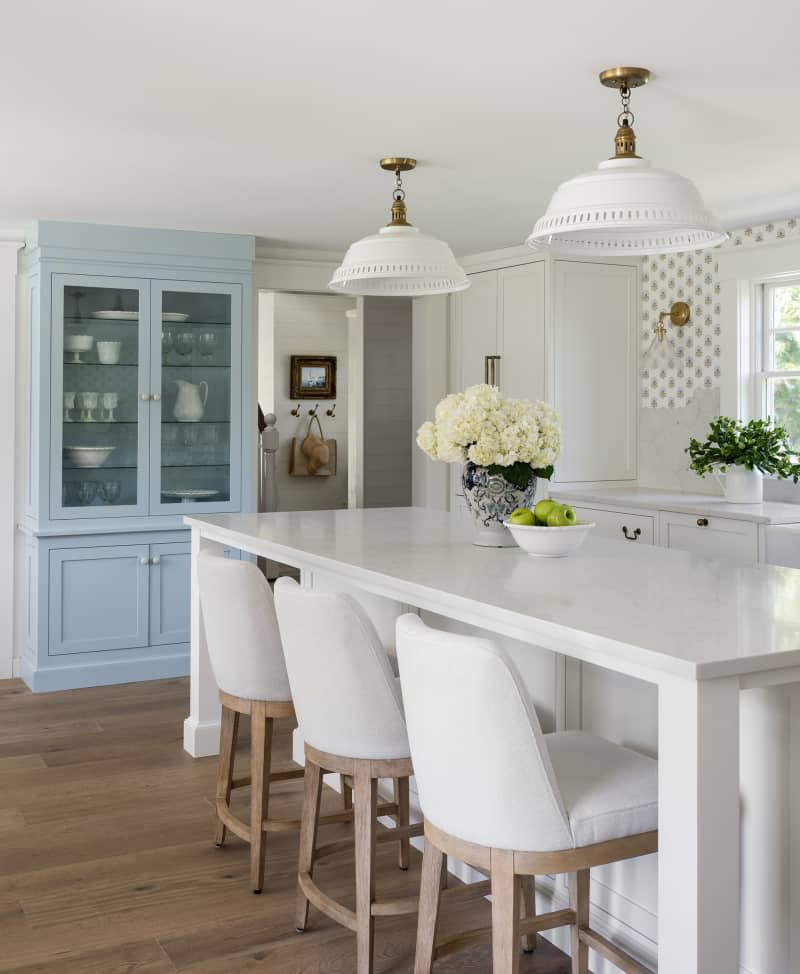White and pale blue kitchen with wallpaper and cushioned white barstools
