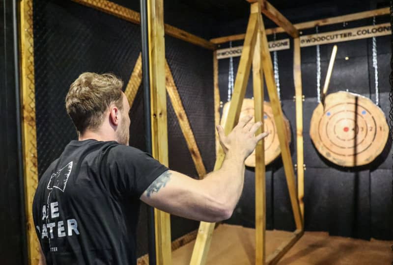 Aron Lack throws an axe at a wooden disc in the WoodCutter axe-throwing bar in Cologne. The sport is accessible to all, with a range of axe sizes and comprehensive safety measures, including fenced lanes and mandatory briefings. Oliver Berg/dpa