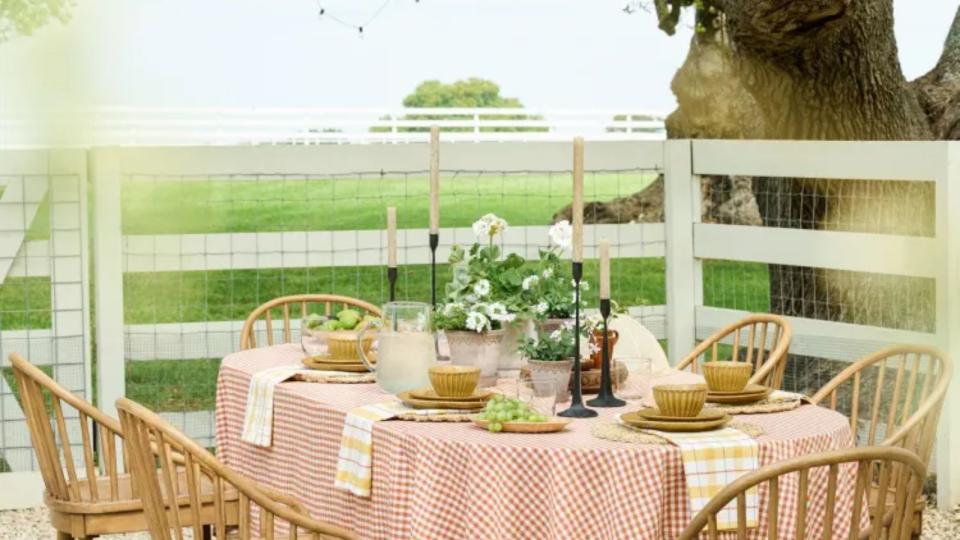 A table outside laid with a gingham tablecloth, tapers, yellow bowls, and napkins