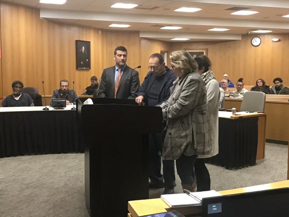 Robert Feirstein, standing and wearing black clothing and glasses, and Rebeckka Mustaffa, standing and wearing plaid coat, speak Dec. 15, 2022 in Macomb County Circuit Court at the sentencing of Henry Johnson, seated far left, in the 2013 stabbing deaths of their niece Kristina (Krissy) Geiger, 11, and Krissy's mother, Tina Geiger, in Clinton Township. Henry Johnson's brother, Tony Johnson, was sentenced separately in the Geigers' deaths after the two brothers were convicted by a jury in October 2022.