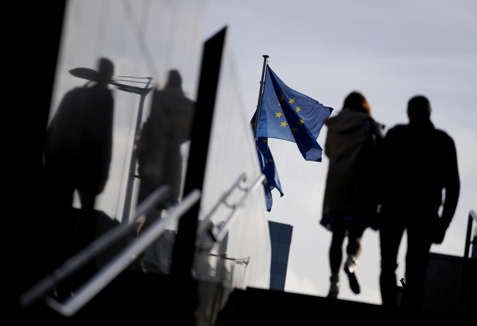 FILE - A couple walk past EU flags outside EU headquarters in Brussels, on Oct. 26, 2021. Police in Italy, Austria, Romania and Slovakia arrested 22 people Thursday as part of an investigation into the suspected siphoning of hundreds millions of euros in post-pandemic relief funds from the European Union. (AP Photo/Virginia Mayo, File)