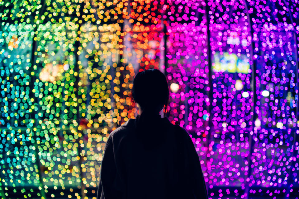 Silhouette of young woman standing against illuminated and colourful bokeh lights background in the city at night