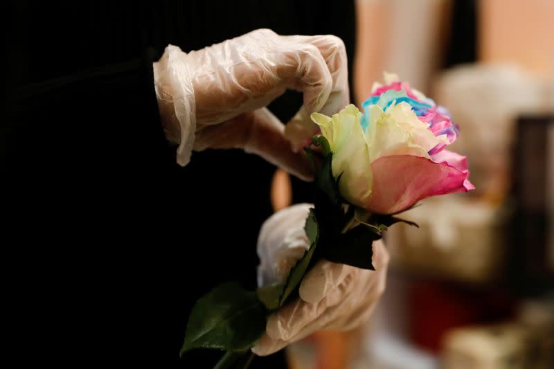 A florist who prefers to be called Cai Xiaoman wearing gloves, holds a rose while she ensembles a bouquet at a flowers shop in a shopping mall, as the country is hit by an outbreak of the new coronavirus, in Beijing