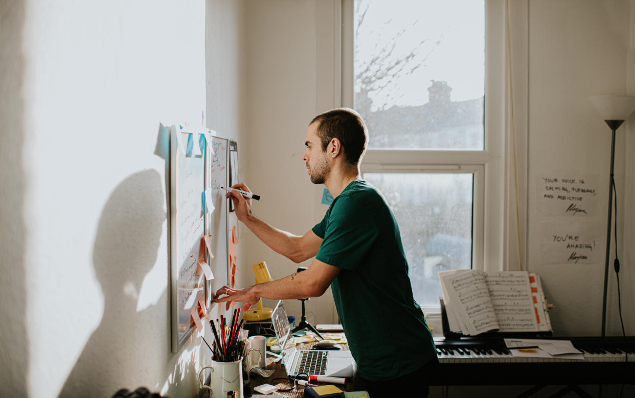 A man in a sunny home office writes on a white board with a marker.