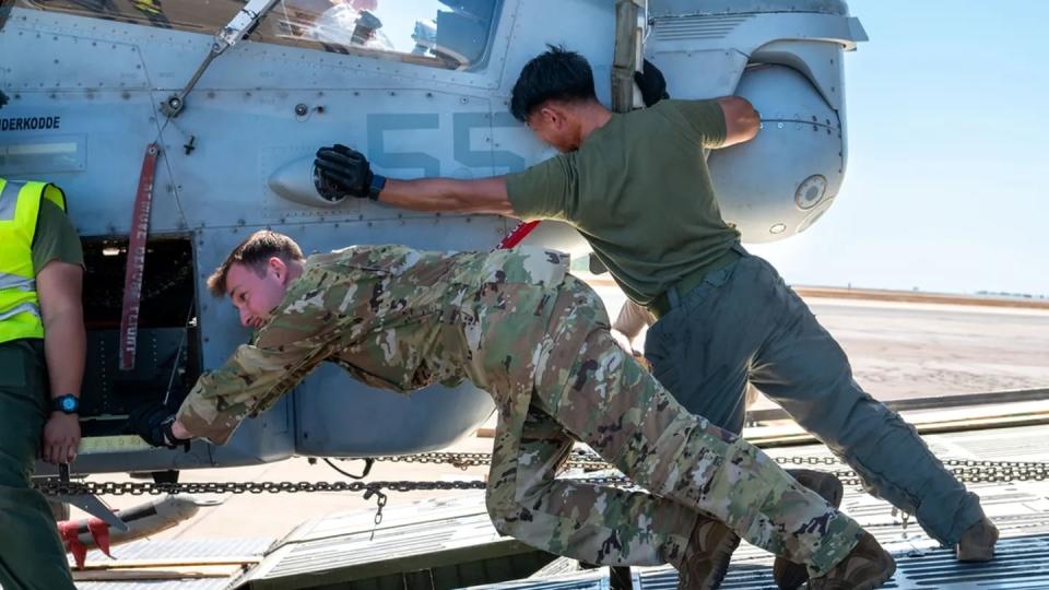 A U.S. airman, left, and a U.S. Marine unload a AH-1Z helicopter from a C-5 Galaxy at Royal Australian Air Force Base Darwin July 13. The C-5 transported two Venom helicopters for Marine Rotational Force Darwin and Exercise Talisman Sabre, which Mobility Guardian participants helped receive and unload. (Airman 1st Class Stassney Davis/Air Force)