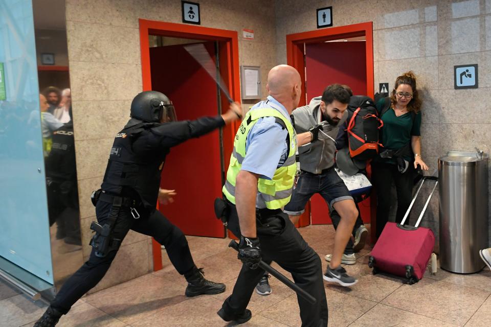 Otro manifestante es reprimido por un agente ante la mirada de una viajera con maleta (Photo by LLUIS GENE/AFP via Getty Images)