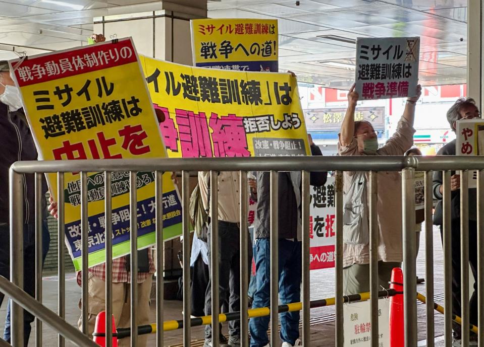 反對飛彈避難訓練的抗議者在日本東京練馬火車站前舉著標語，上面寫著「中止飛彈避難訓練」、「飛彈避難訓練是戰爭準備」。路透社