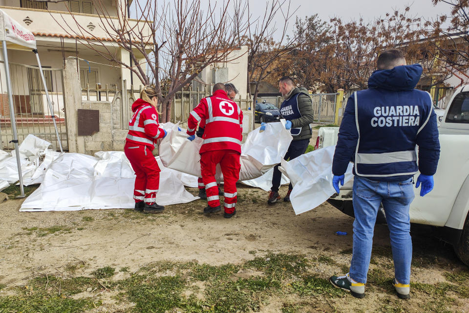Italian Red Cross volunteers and coast guards carry bags containing the bodies of migrants who died when their overcrowded wooden boat smashed into rocky reefs, at a beach near Cutro, southern Italy, Sunday, Feb. 26, 2023. Rescue officials say an undetermined number of migrants have died and dozens have been rescued after their boat broke apart off southern Italy. (Antonino Durso/LaPresse via AP)