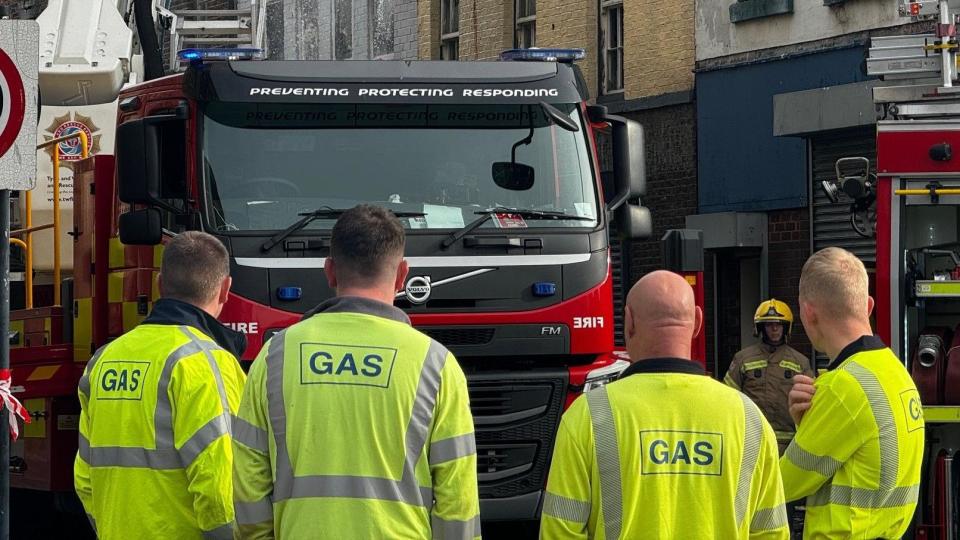 Four gas workers in high visibility vests in front of a fire engine
