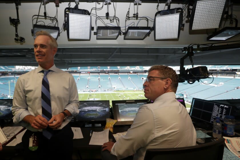 In this Friday, Aug. 23, 2019, photo, Fox Sports play-by-play announcer Joe Buck, left, and analyst Troy Aikman, right, work in the broadcast booth before a preseason NFL football game between the Miami Dolphins and Jacksonville Jaguars, in Miami Gardens, Fla. The exhibition game served as a dress rehearsal for the Fox Sports crew for the upcoming Super Bowl to be hosted by Miami in 2020. (AP Photo/Lynne Sladky)