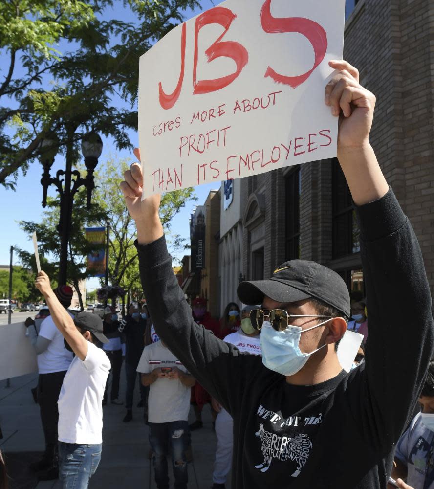 A group of people hold up signs at a protest. The sign in the foreground reads ‘JBS cares more about profit than its employees’.