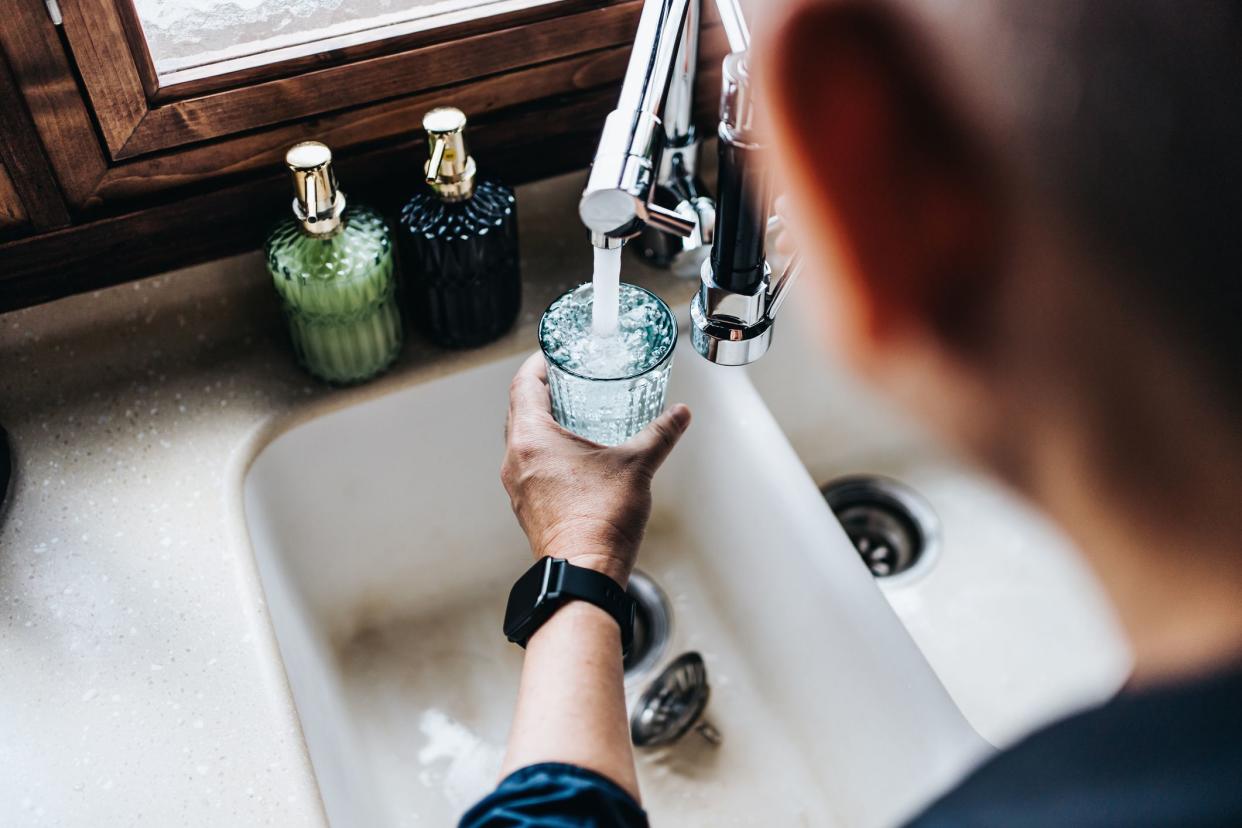 Over the shoulder view of senior Asian man filling a glass of filtered water right from the tap in the kitchen at home