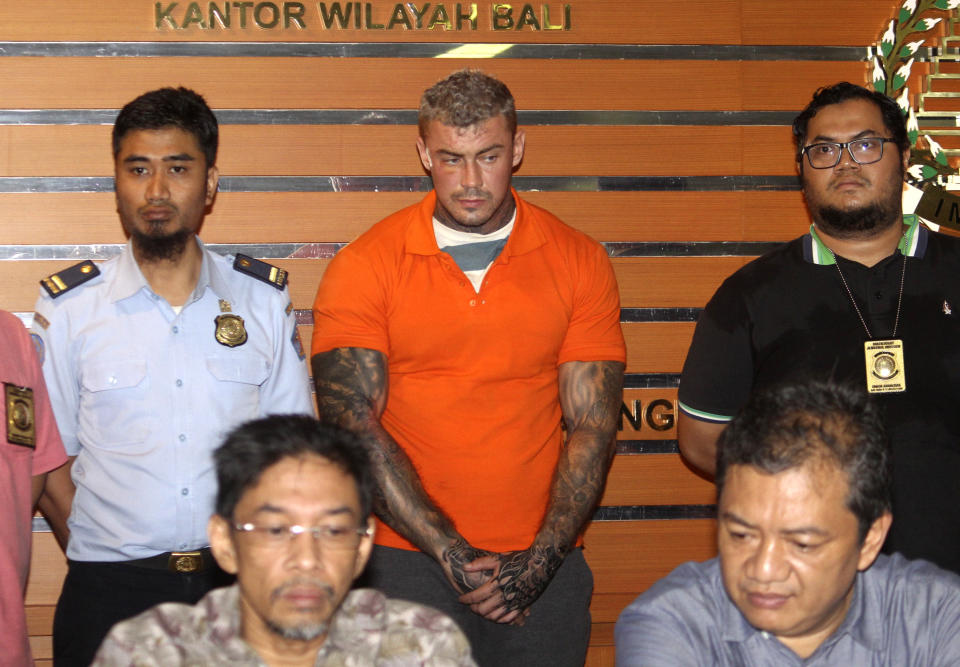 Immigration officers flank British national Terence Murrell, center, as he is presented to the media during a press conference in Bali, Indonesia, Tuesday, July 30, 2019. Indonesian authorities say they arrested the alleged British fugitive in Bali in possession of pornography and drugs. (AP Photo/Yoan Ari)