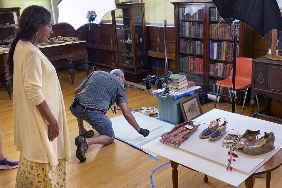 FILE - Leola One Feather, left, of the Oglala Sioux Tribe in South Dakota, observes as John Willis photographs Native American artifacts on July 19, 2022, at the Founders Museum in Barre, Mass. Federal penalties have increased under a newly signed law Wednesday, Dec. 21, 2022, intended to protect the cultural patrimony of Native American tribes. (AP Photo/Philip Marcelo, File)