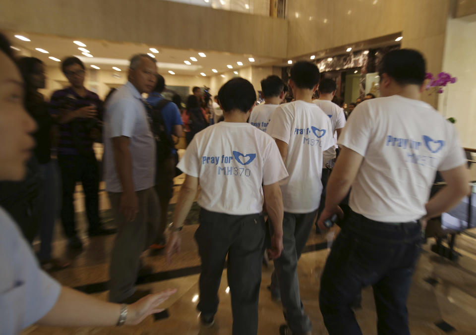 Newly arrived Chinese relatives of passengers on board the missing Malaysia Airlines flight MH370 are escorted inside a hotel in Subang Jaya, Malaysia, Sunday March 30, 2014. Several dozen Chinese relatives of passengers on Flight 370 arrived in Malaysia Sunday to demand more information about what happened to the airliner that has been missing for more than three weeks, saying there has not been enough information on what happened to their loved ones. The shirts worn by the relatives read: "Praying that MH370 returns home safely." (AP Photo/Aaron Favila)