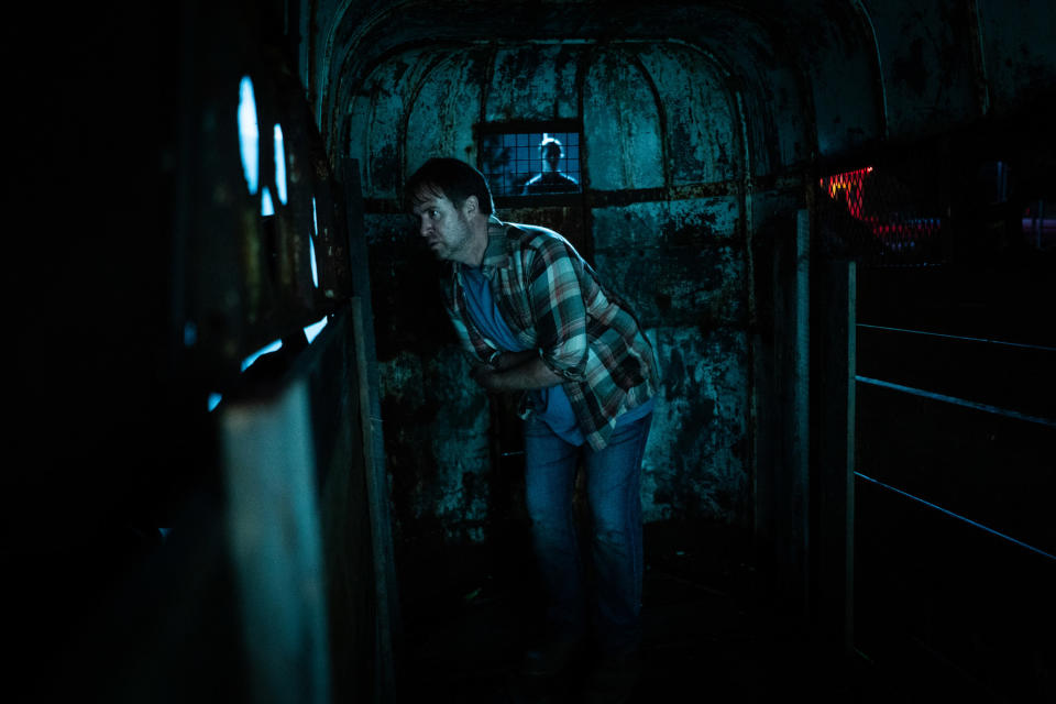 A man is locked in a trailer surrounded by humanoid monsters at night