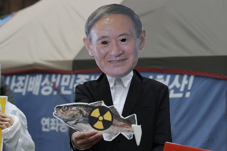 An environmental activist wearing a mask of Japanese Prime Minister Yoshihide Suga performs to denounce the Japanese government's decision near the Japanese embassy in Seoul, South Korea, Tuesday, April 13, 2021. Japan's government decided Tuesday to start releasing massive amounts of treated radioactive water from the wrecked Fukushima nuclear plant into the Pacific Ocean in two years - an option fiercely opposed by local fishermen and residents. (AP Photo/Lee Jin-man)