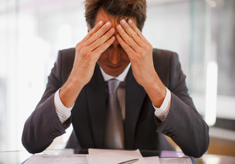 Man in suit sitting at a desk and holding his forehead in his hands.