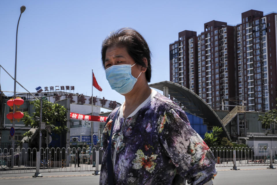 A woman wearing a protective face mask to help curb the spread of the new coronavirus walks by the seafood wholesale market closed for inspection in Beijing, Sunday, June 14, 2020. China is reporting its highest daily total of coronavirus cases in two months after the capital's biggest wholesale food market was shut down following a resurgence in local infections. (AP Photo/Andy Wong)