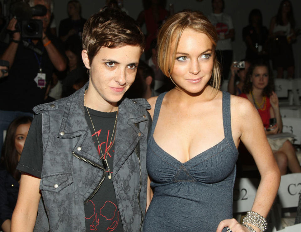 Samantha Ronson and Lindsay Lohan pose together at an event. Samantha wears a casual vest and t-shirt, while Lindsay is in a sleeveless dress