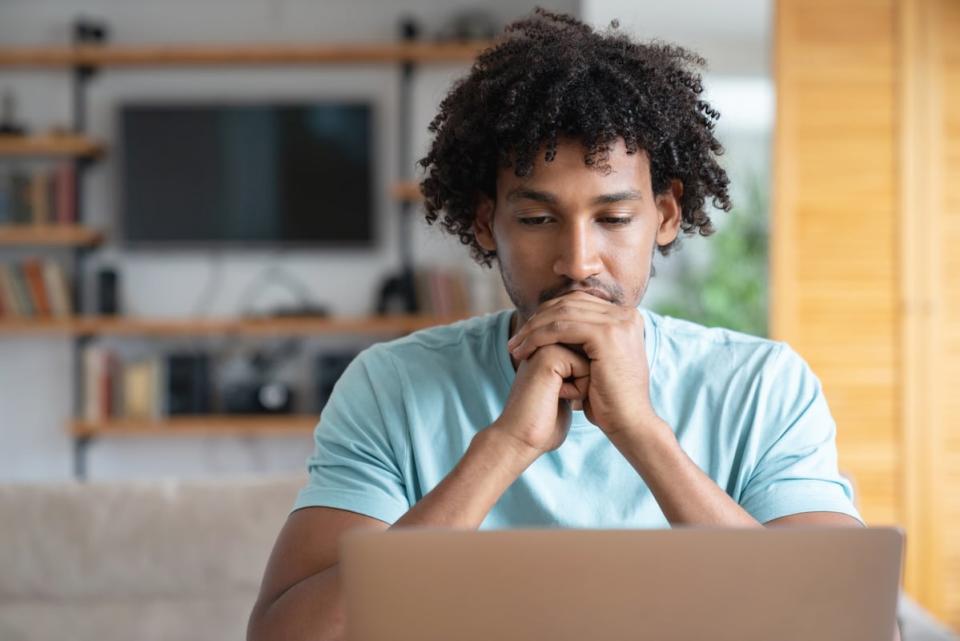 A person clasps their hands while sitting in front of a laptop computer. 