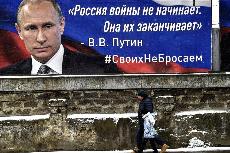 Gente pasando frente a un cartel de Vladimir Putin que dice 