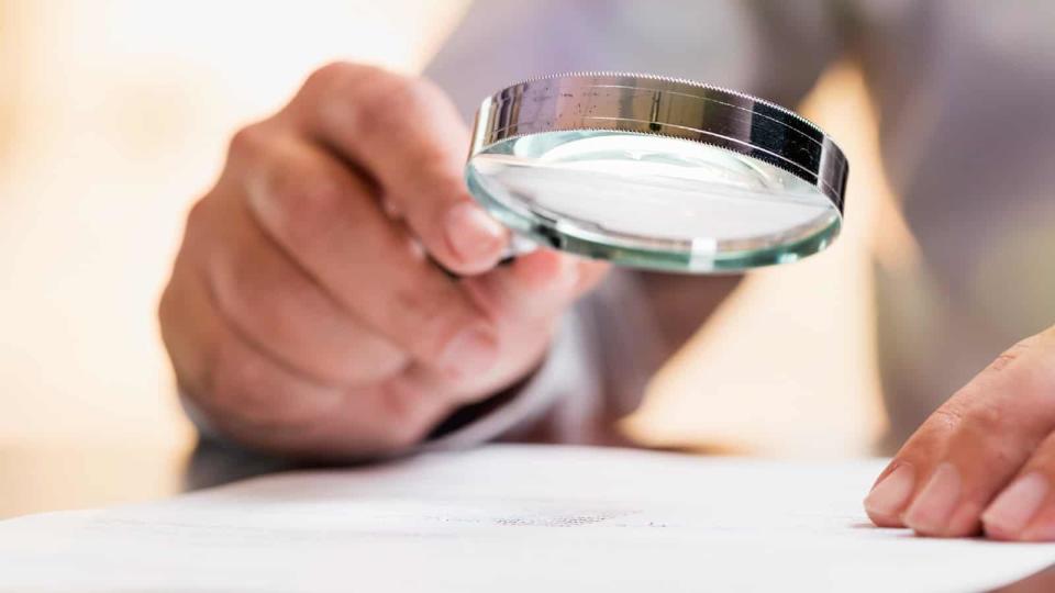 Person holds magnifying glass over important document and reads the small print