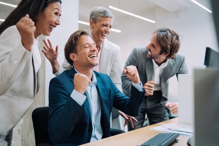 A group of investors cheers in front of a computer in an office.