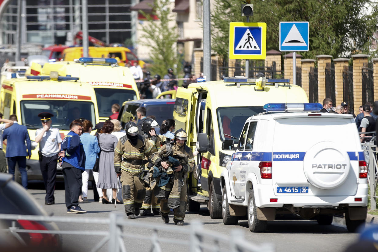 Firefighters walk past ambulances and police cars and a truck parked at a school after a shooting in Kazan, Russia, Tuesday, May 11, 2021. Russian media report that several people have been killed and wounded in a school shooting in the city of Kazan. Russia's state RIA Novosti news agency reported the shooting took place Tuesday morning, citing emergency services. (AP Photo/Roman Kruchinin)