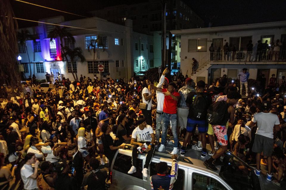 Crowds gather in the street while a speaker blasts music an hour past curfew in Miami Beach, Fla., on Sunday, March 21, 2021. An 8 p.m. curfew has been extended in Miami Beach after law enforcement worked to contain unruly crowds of spring break tourists. (Daniel A. Varela/Miami Herald via AP)