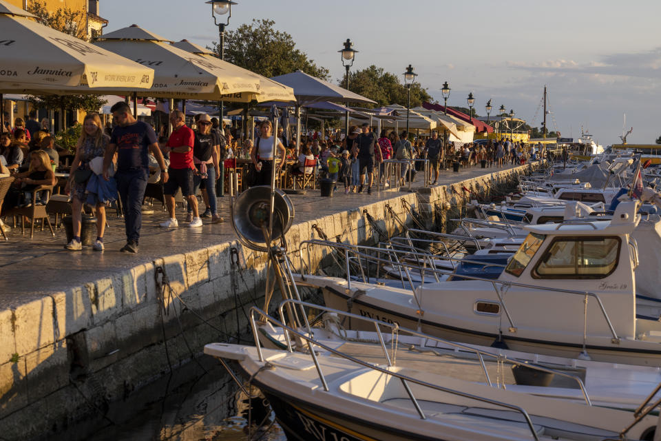 Holidaymakers walk by the harbor, in the Adriatic town of Rovinj, Croatia, Friday, Aug. 27, 2021. Summer tourism has exceeded even the most optimistic expectations in Croatia this year. Beaches along the country's Adriatic Sea coastline are swarming with people. Guided tours are fully booked, restaurants are packed and sailboats were chartered well in advance. (AP Photo/Darko Bandic)