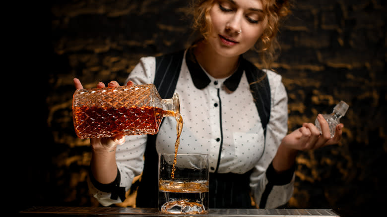 A bartender pouring a glass of whiskey from a decanter