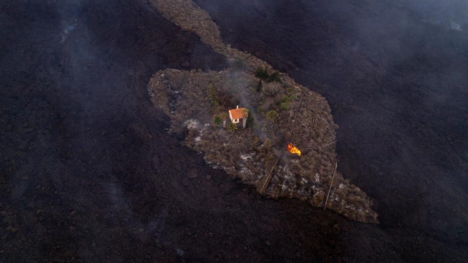 Sept. 20, 2021: In this photo provided by iLoveTheWorld, a house remains intact as lava flows after a volcano erupted near Las Manchas on the island of La Palma in the Canaries, Spain. A dormant volcano on a small Spanish island in the Atlantic Ocean erupted on Sunday, forcing the evacuation of thousands of people. Huge plumes of black-and-white smoke shot out from a volcanic ridge where scientists had been monitoring the accumulation of molten lava below the surface.