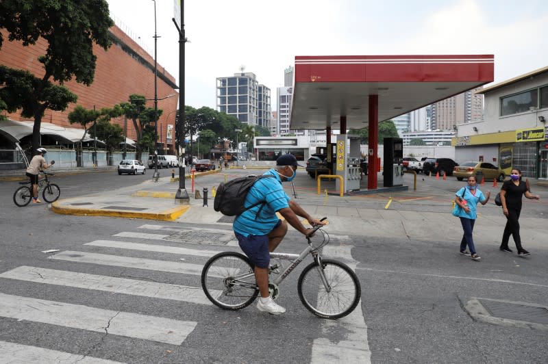 People riding bicycles pass in front of a closed gas station in Caracas