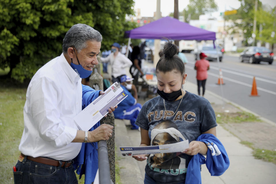 Philadelphia District Attorney candidate Carlos Veg, left, gives a campaign pamphlet to Keila Cruz, of North Philadelphia, during an anti-violence rally at Clara Muhammad Square in West Philadelphia on Saturday, May 15, 2021. Vega is running against incumbent Larry Krasner in the Democratic primary May 18. (Tim Tai/The Philadelphia Inquirer via AP)