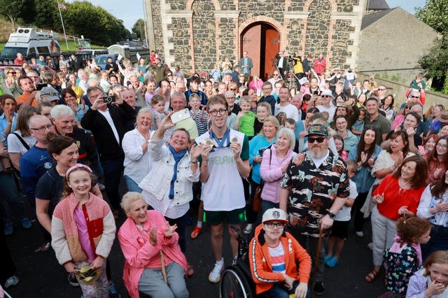 A man holds his gold medals surrounded by a crowd of people 