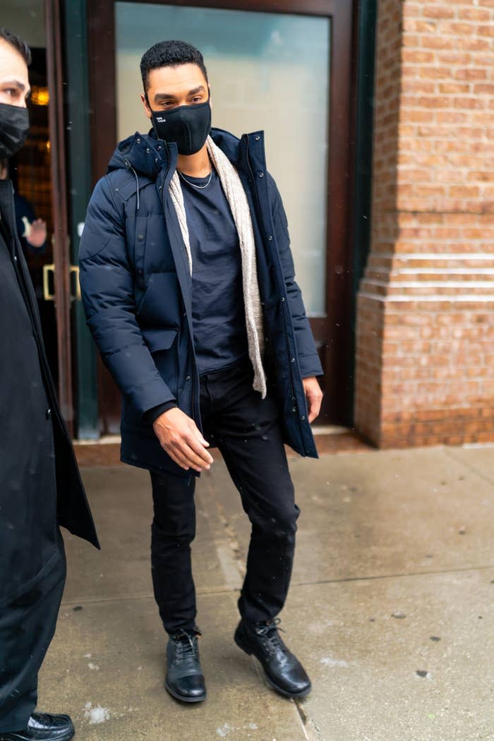 Regé-Jean Page walking out of a building with a face mask and a puffer jacket
