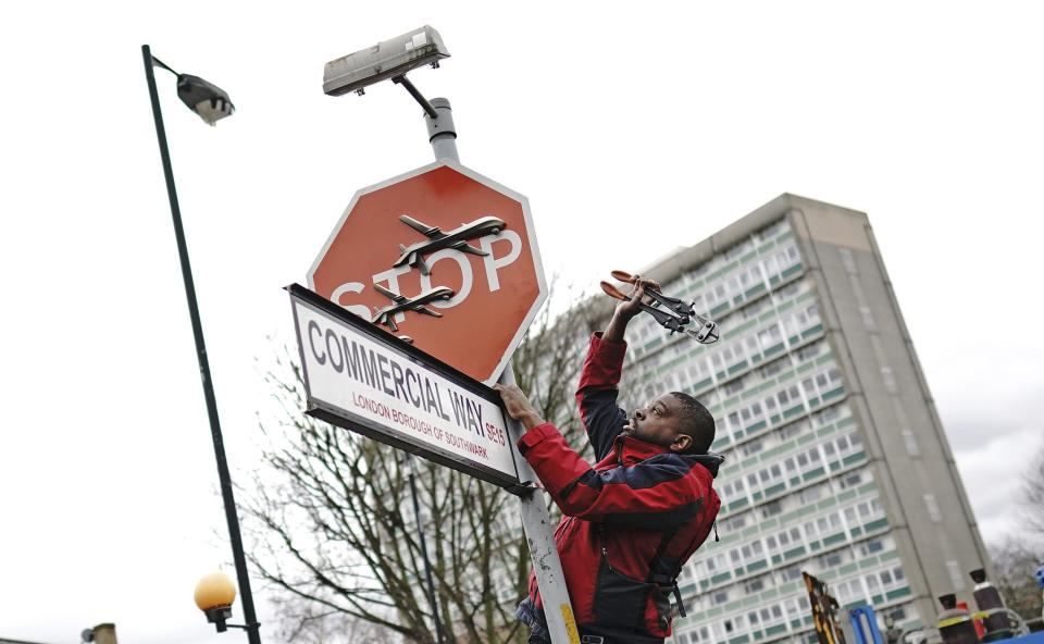 A person removes a piece of art work by Banksy, which shows what looks like three drones on a traffic stop sign, which was unveiled at the intersection of Southampton Way and Commercial Way in Peckham, south east London, Friday Dec. 22, 2023. (Aaron Chown/PA via AP)