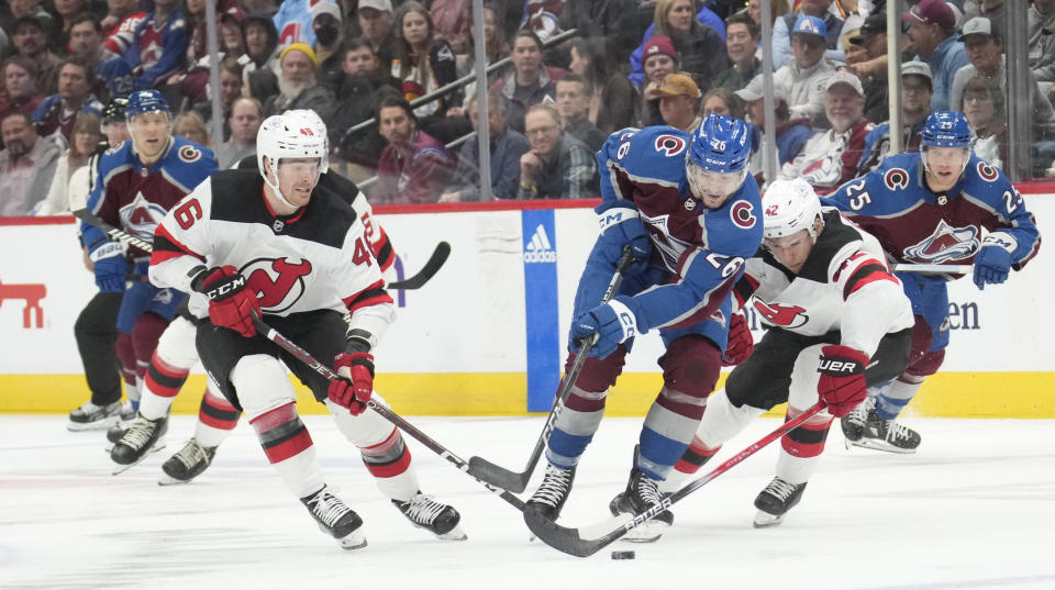 Colorado Avalanche center Ondrej Pavel (26) drives between New Jersey Devils center Max Willman, left, and center Curtis Lazar in the third period of an NHL hockey game on Tuesday, Nov. 7, 2023, in Denver. (AP Photo/David Zalubowski)