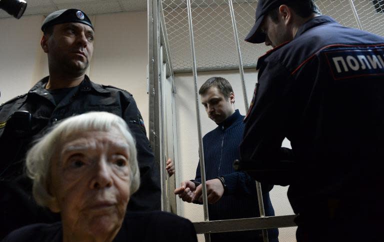 Mikhail Kosenko, one of the activists accused of violence at a rally, stands in a defendant's cage in a court in Moscow on October 8, 2013, as Moscow Helsinki Group president Lyudmila Alekseyeva (front) attends the trial