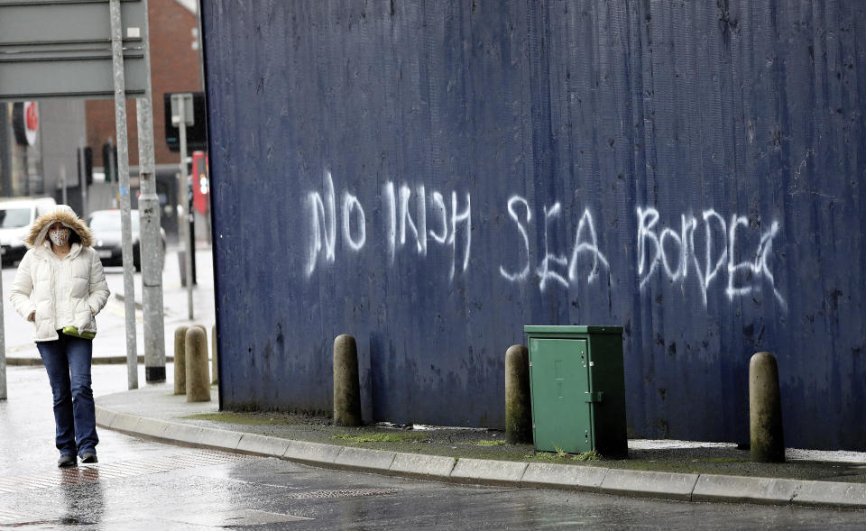 FILE - In this Wednesday, Feb. 3, 2021 file photo, a woman walks past past graffiti with the words 'No Irish Sea Border' in Belfast city centre, Northern Ireland. The schism of Brexit has crystalized in the worsening fight over Northern Ireland, the only part of the U.K. to share a land border with an EU country. Under the most delicate and contentious part of the Brexit deal, Northern Ireland remains inside the EU's single market for trade in goods, in order to avoid a hard border with EU member Ireland. (AP Photo/Peter Morrison, File)