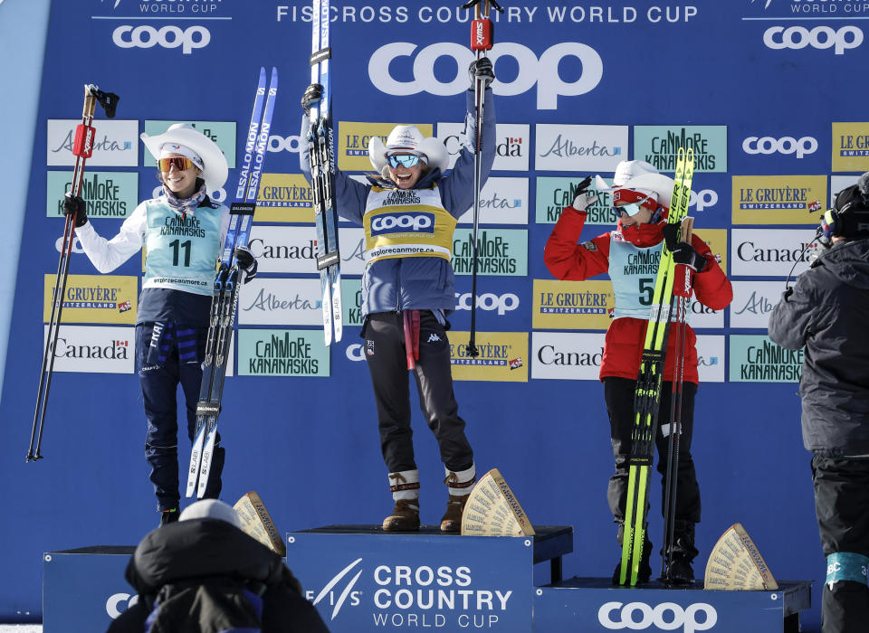 Jessie Diggins, center, of the United States, celebrates her victory with second place finisher France's Delphine Claudel, left, and third place finisher Norway's Heidi Weng on the podium following the women's 15km Mass Start freestyle World Cup cross country skiing event in Canmore, Alberta, Friday, Feb. 9, 2024. (Jeff McIntosh/The Canadian Press via AP)