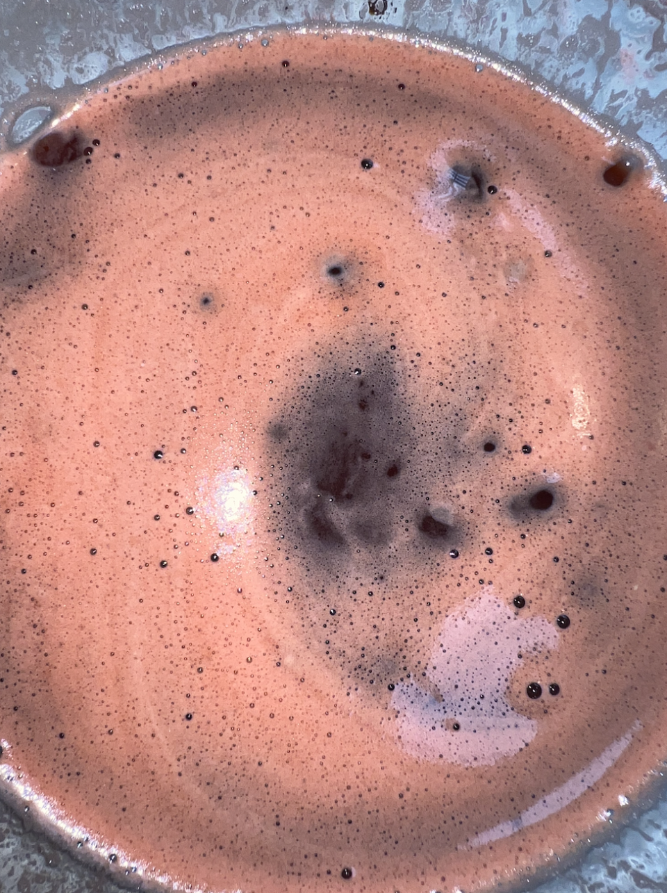 A close-up view of a frothy, mixed beverage with particles and bubbles floating on the surface